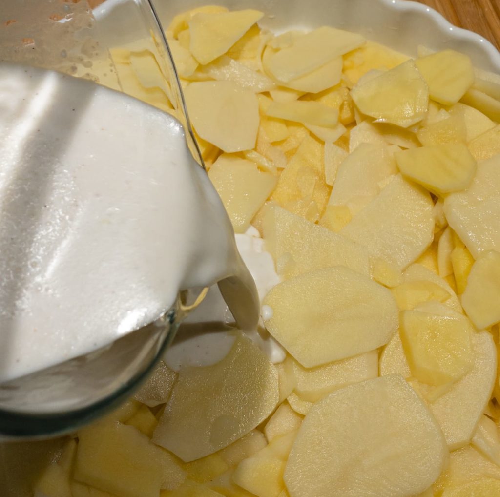 Sliced potatoes in a form, sauce being poured into the form
