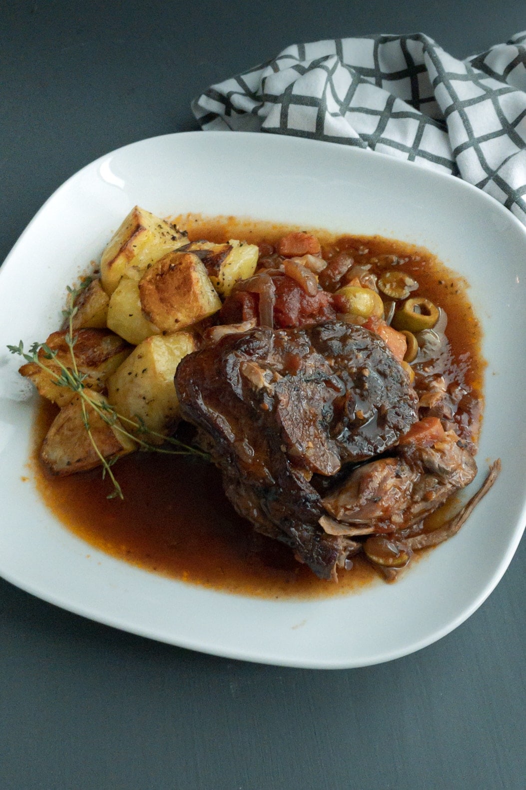 Roasted piece of lamb leg on vegetables in a red wine tomato sauce, served with roasted potatoes