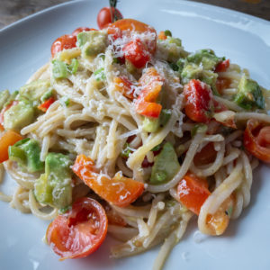 Spaghetti with avocado, bell pepper and and cherry tomatoes on a white plate - featured image