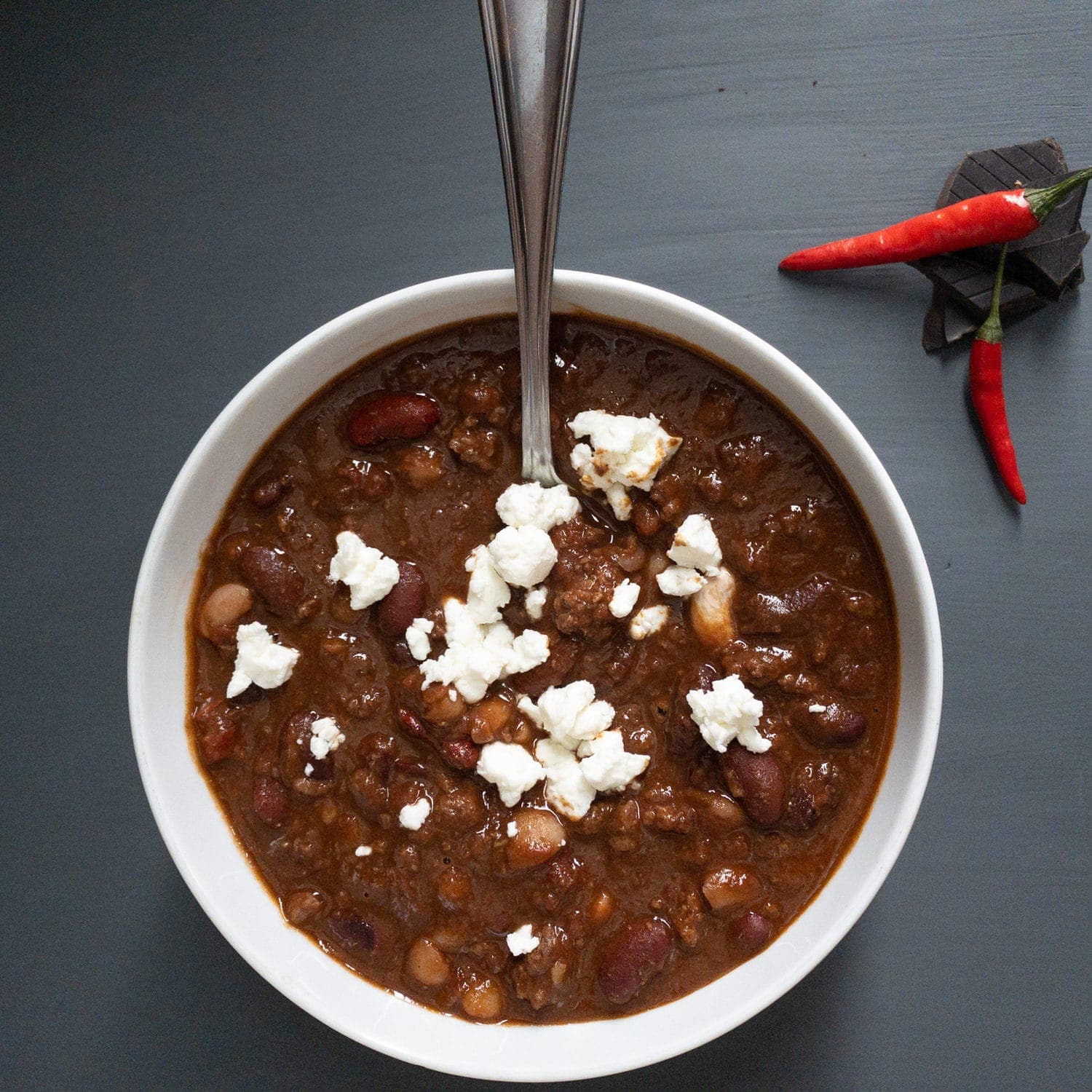 Smoky Chili con Carne in a bowl with a chili and chocolate decoration and feta topping
