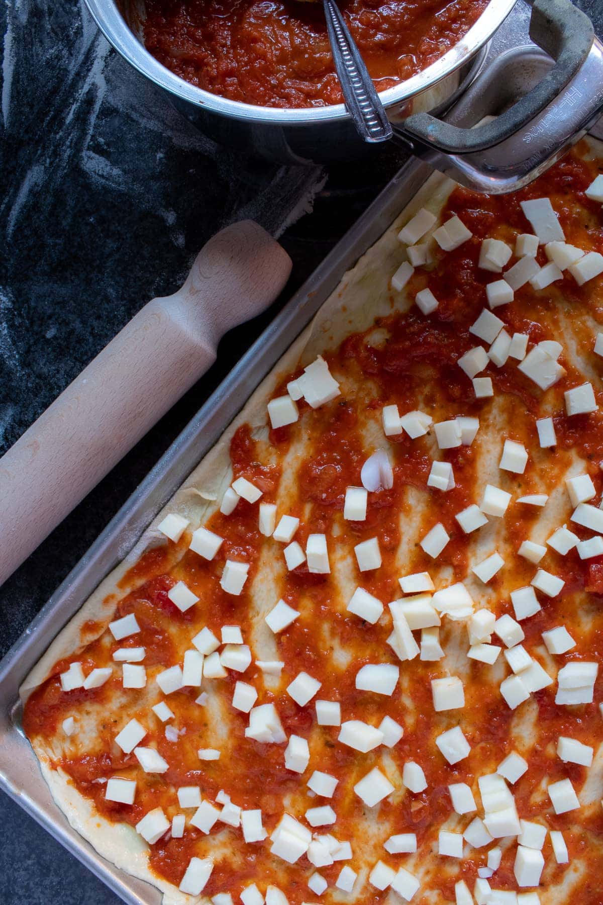 Pizza dough unbaked topped with tomato sauce and diced mozzarella