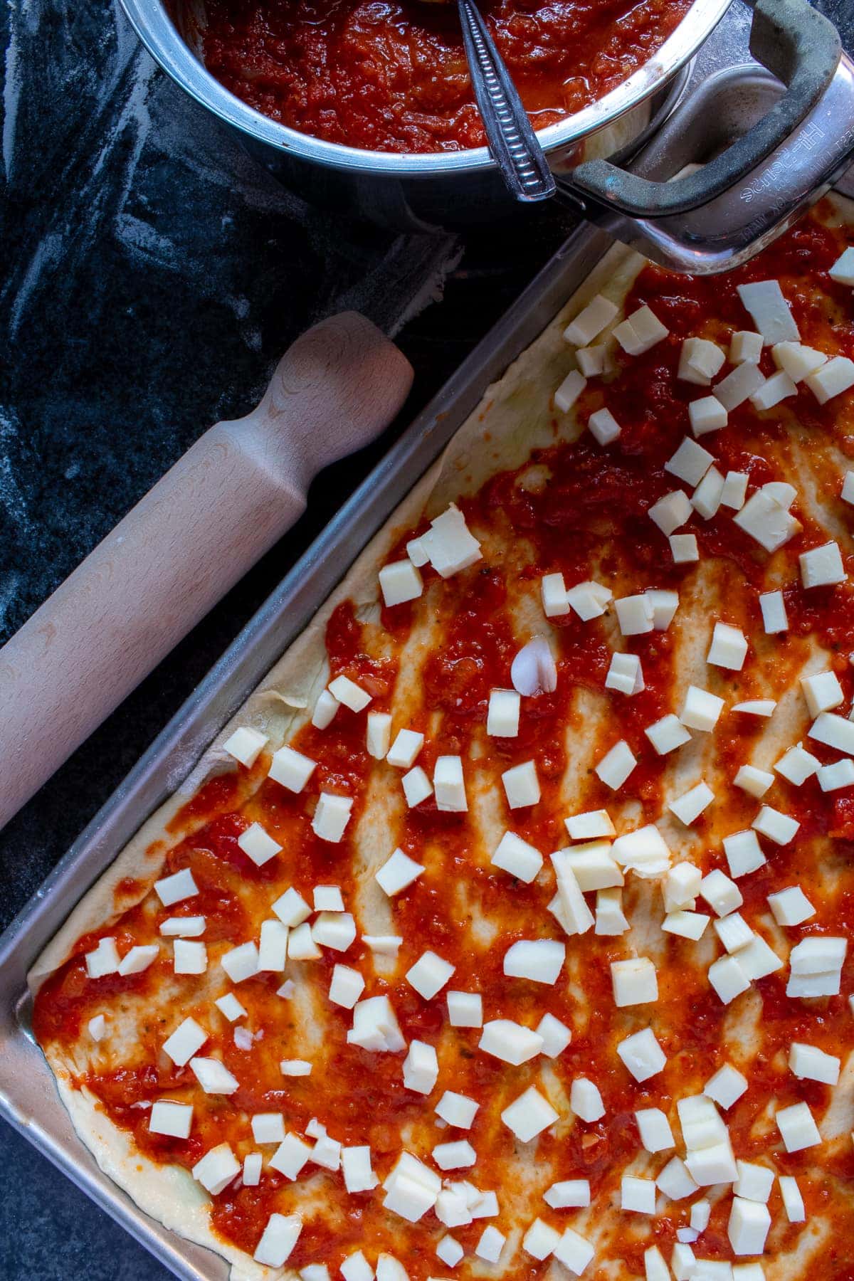 Pizza Sauce on uncooked Pizza Dough, topped with diced Mozzarella