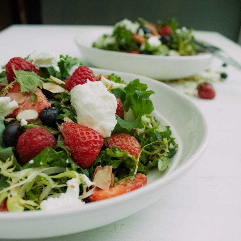 2 plates of kale salad with berries and goat cheese