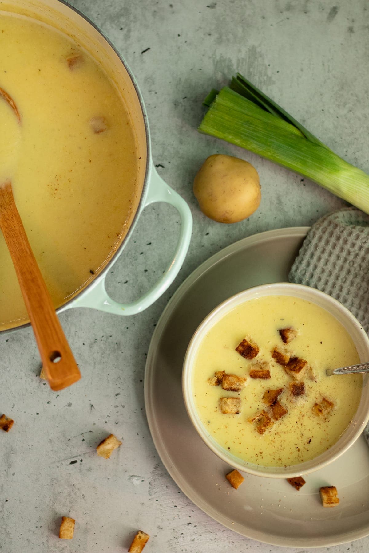 bowl of leek and potato soup with croutons and a pot with soup on the left from it