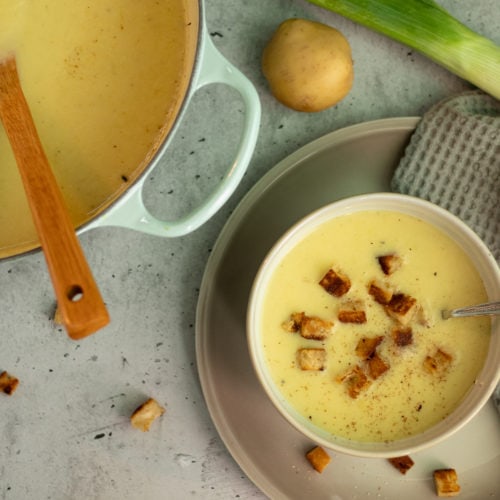 bowl of leek and potato soup with croutons and a pot with soup on the left from it