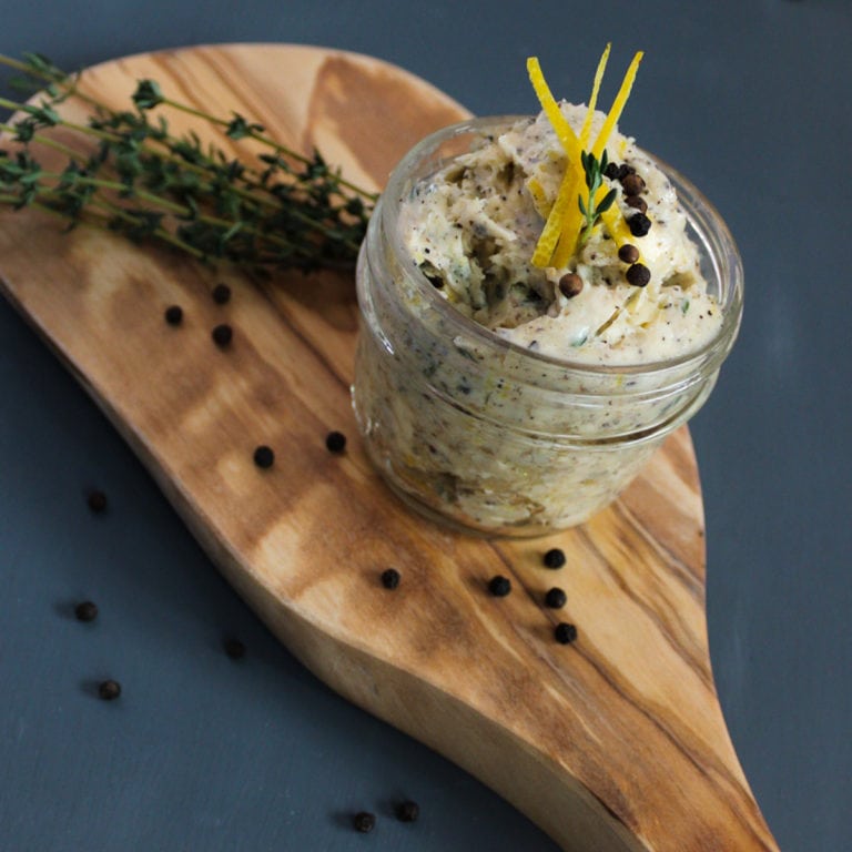 Garlic butter in a jar on a wooden board, garnished with Thyme and lemon zest