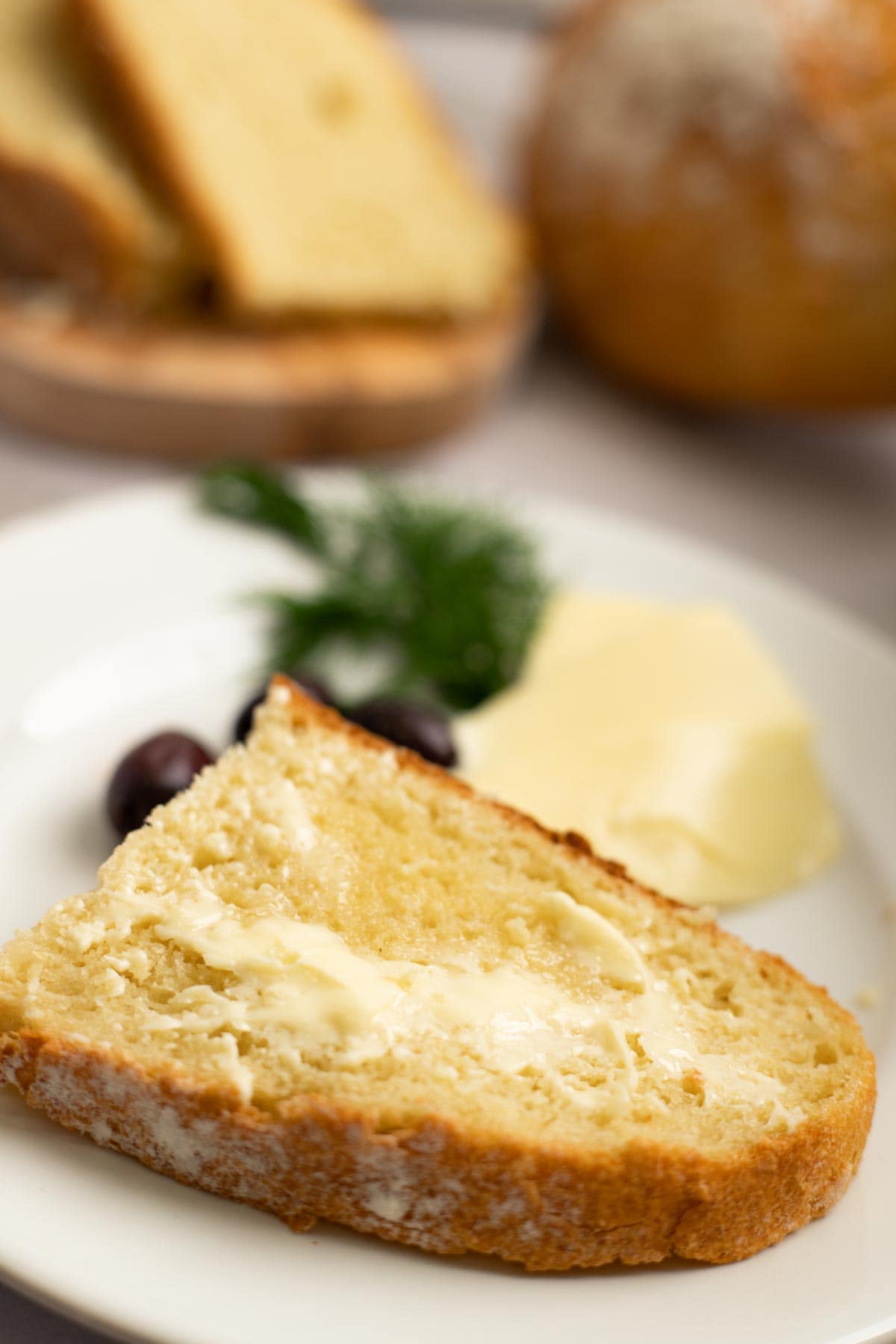 Slice of semolina bread with butter on a white plate with olives and butter.