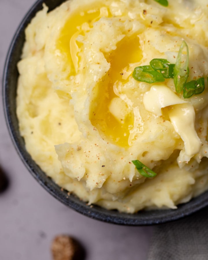 a bowl of mashed potatoes decorated with chopped green onions melted butter and 2 nutmegs next to the bowl.