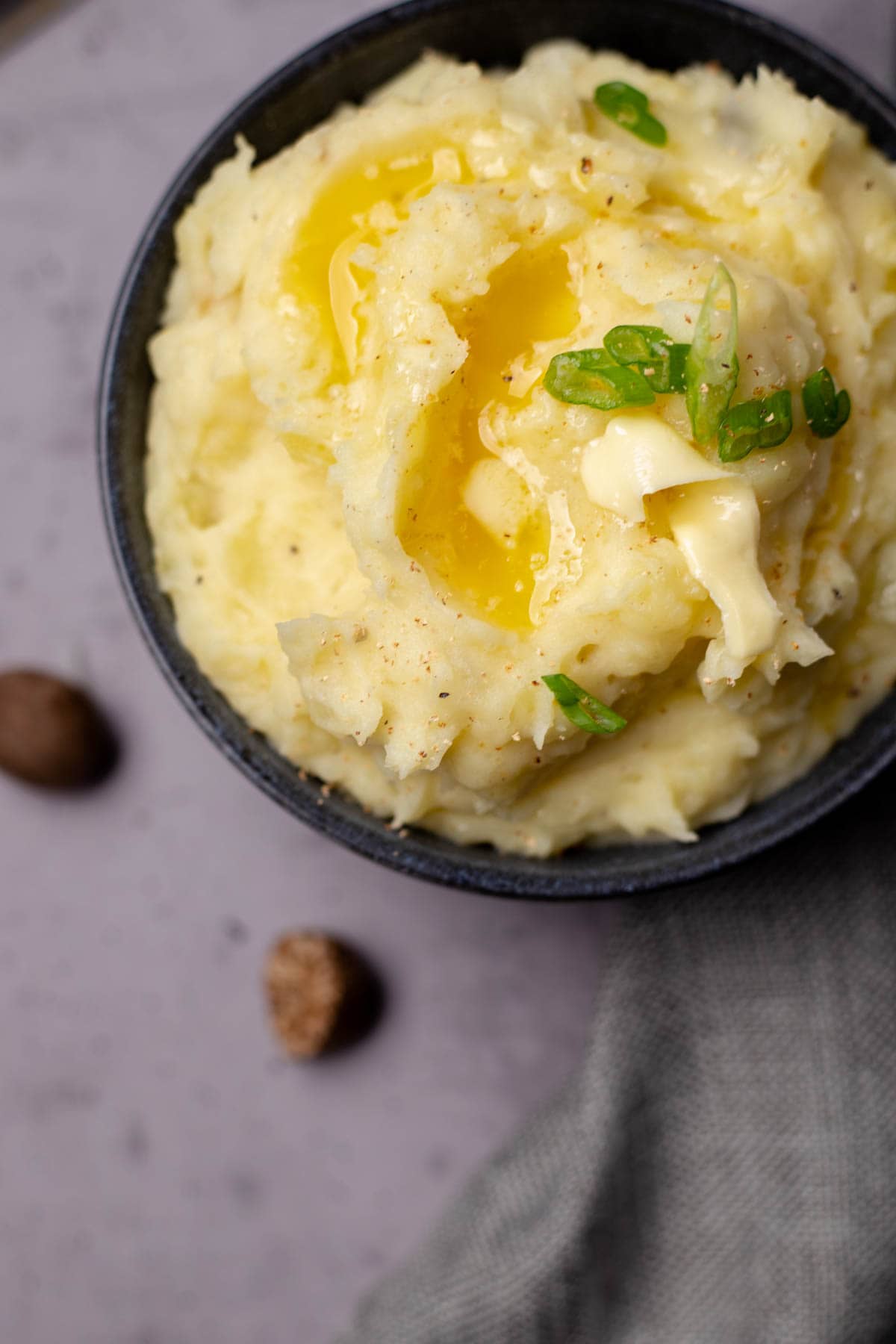 Mashed potatoes in a bowl garnished with ground nutmeg, butter and 2 nutmegs on the side of the bowl.