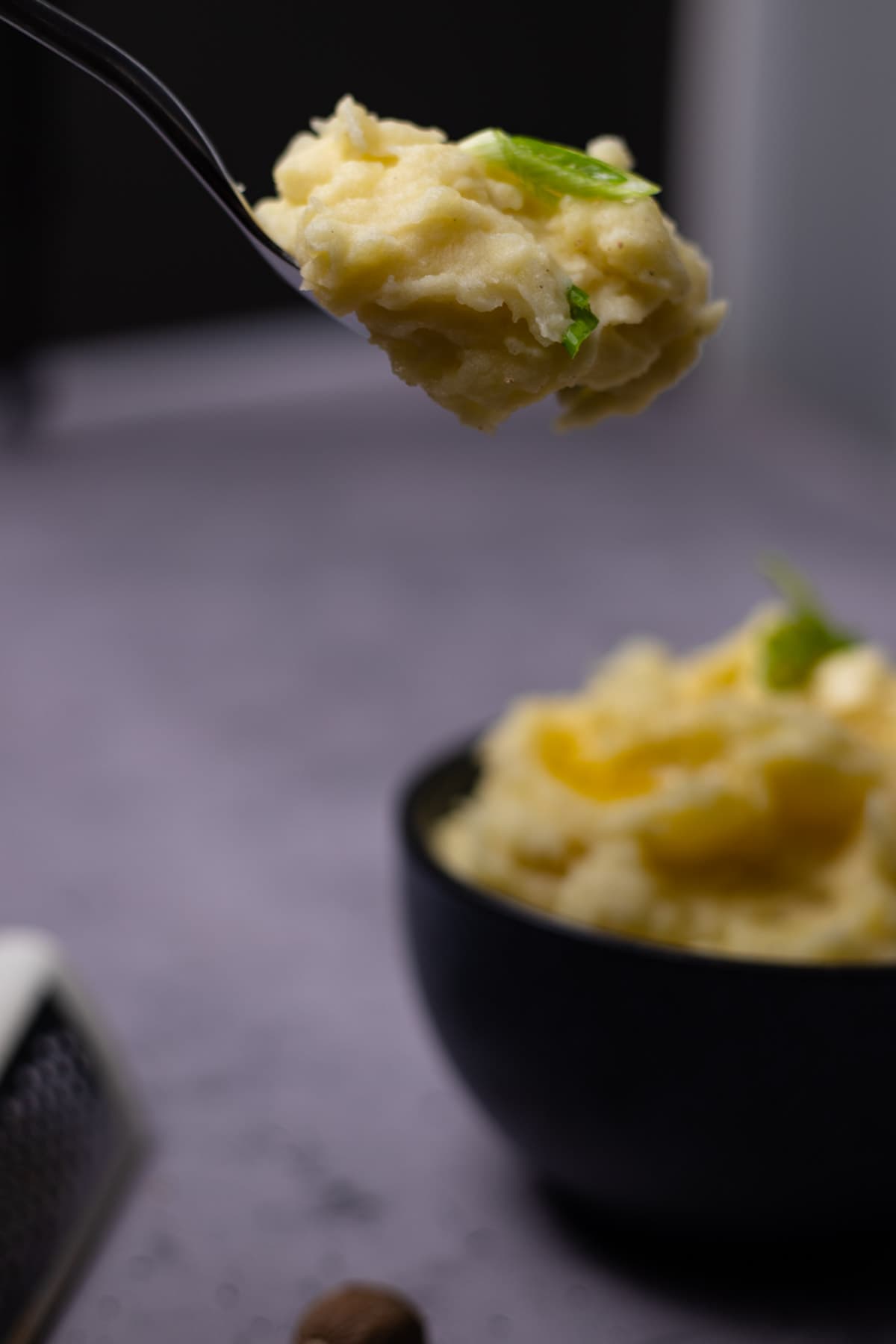 mashed potatoes on a spoon with a bowl blurred in the background.