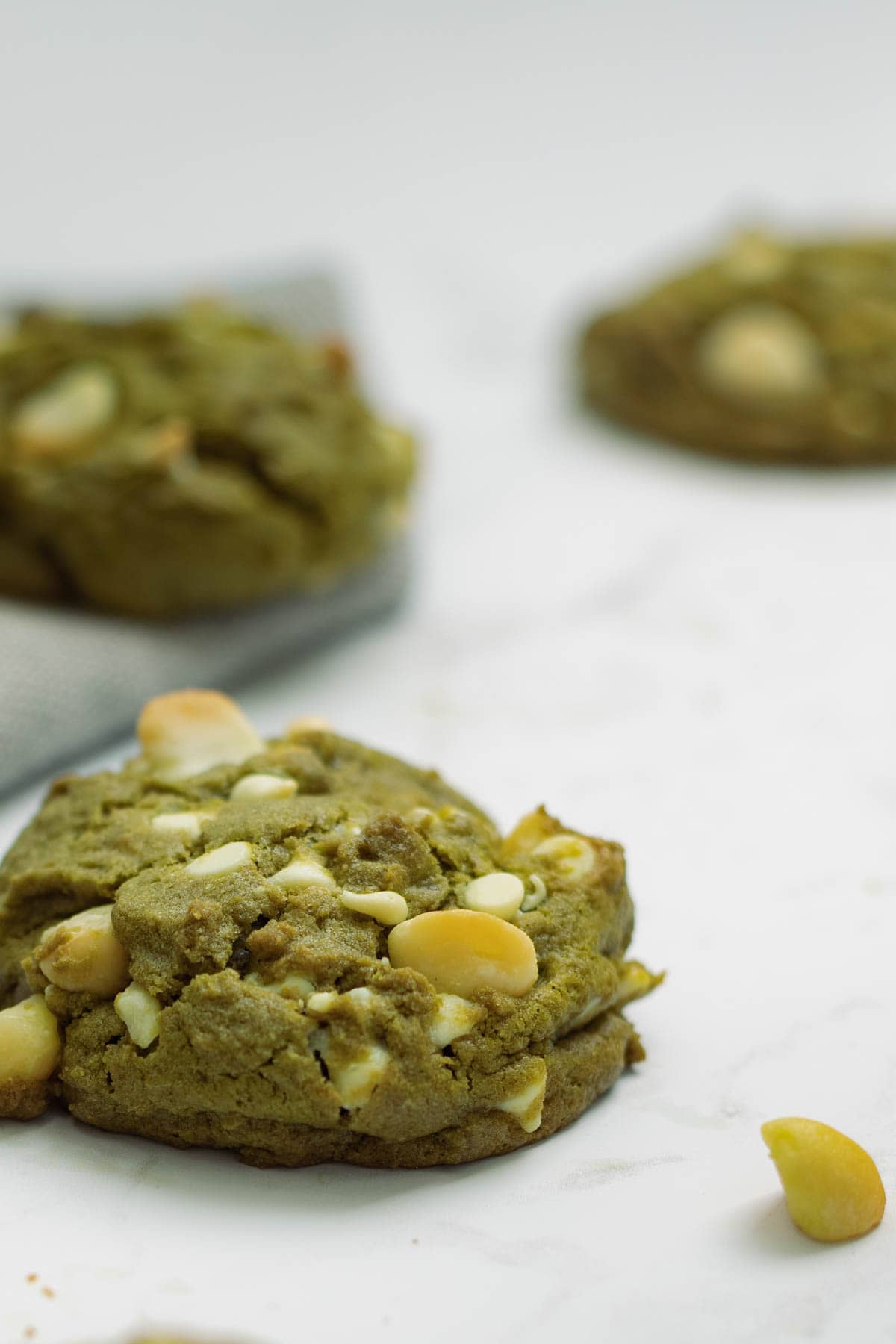 A Matcha Cookie on front left in focus - two cookies blurred out in the back