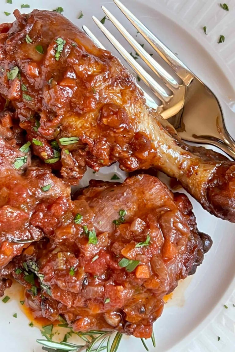Chicken Cacciatore legs on a white plate with a fork on the left side.